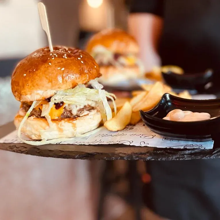 Burger u brioche pecivu na drvenoj dasci, uz njega krumpirići i umak